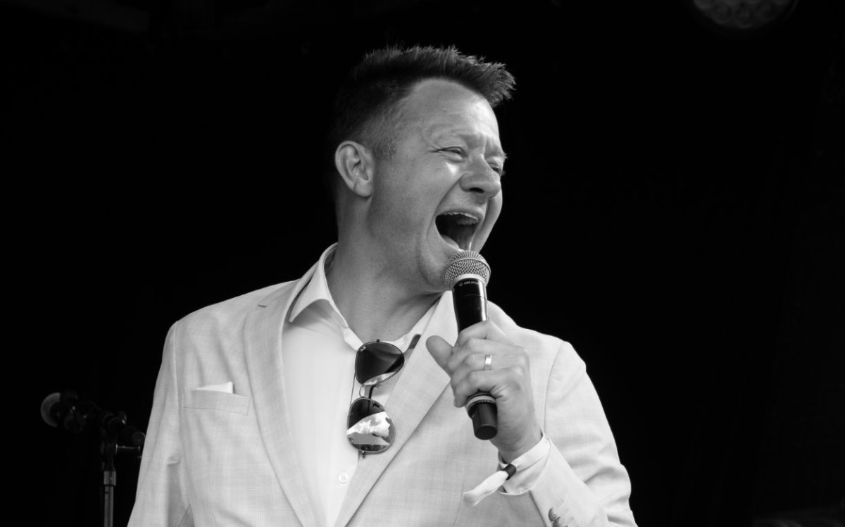 Lars Godbersen, konferencier og foredragsholder, på scenen i lys habit med mikrofon