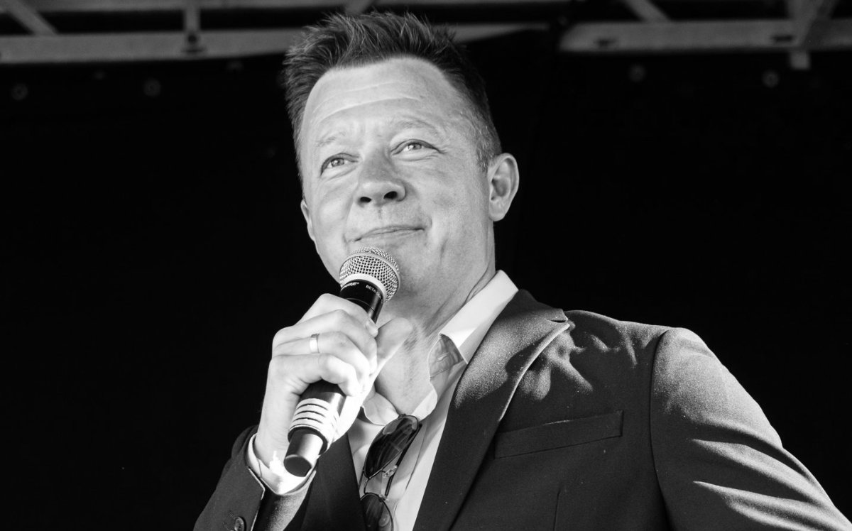 Lars Godbersen, konferencier og foredragsholder, på scenen i mørk habit med mikrofon